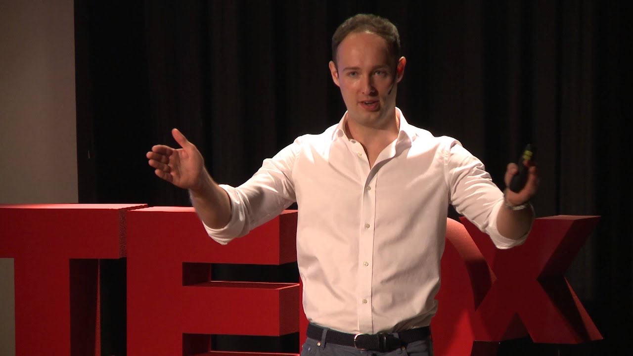 Martynas Kairys on stage at TEDxLugano, arms open, in front of the red TEDx letters